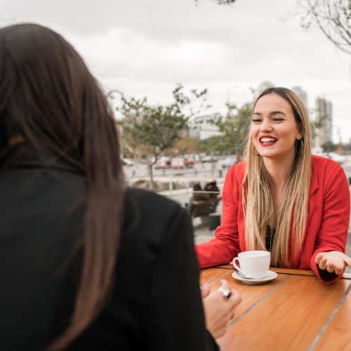 Two cheerful ladies talking while having coffee - Conversational English course for fluency and native-like expression.